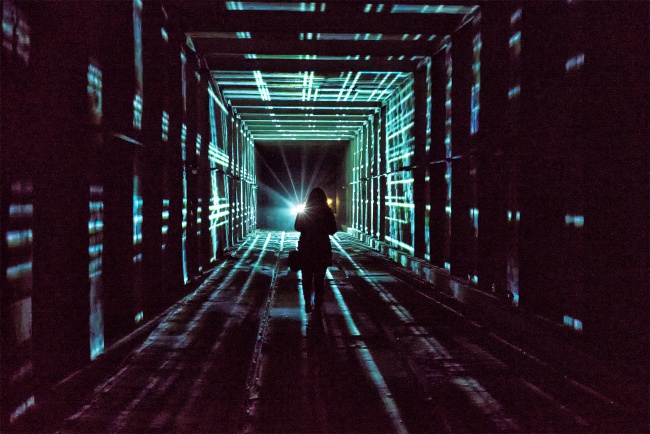 A visitor walking through a tunnel washed in projected light
