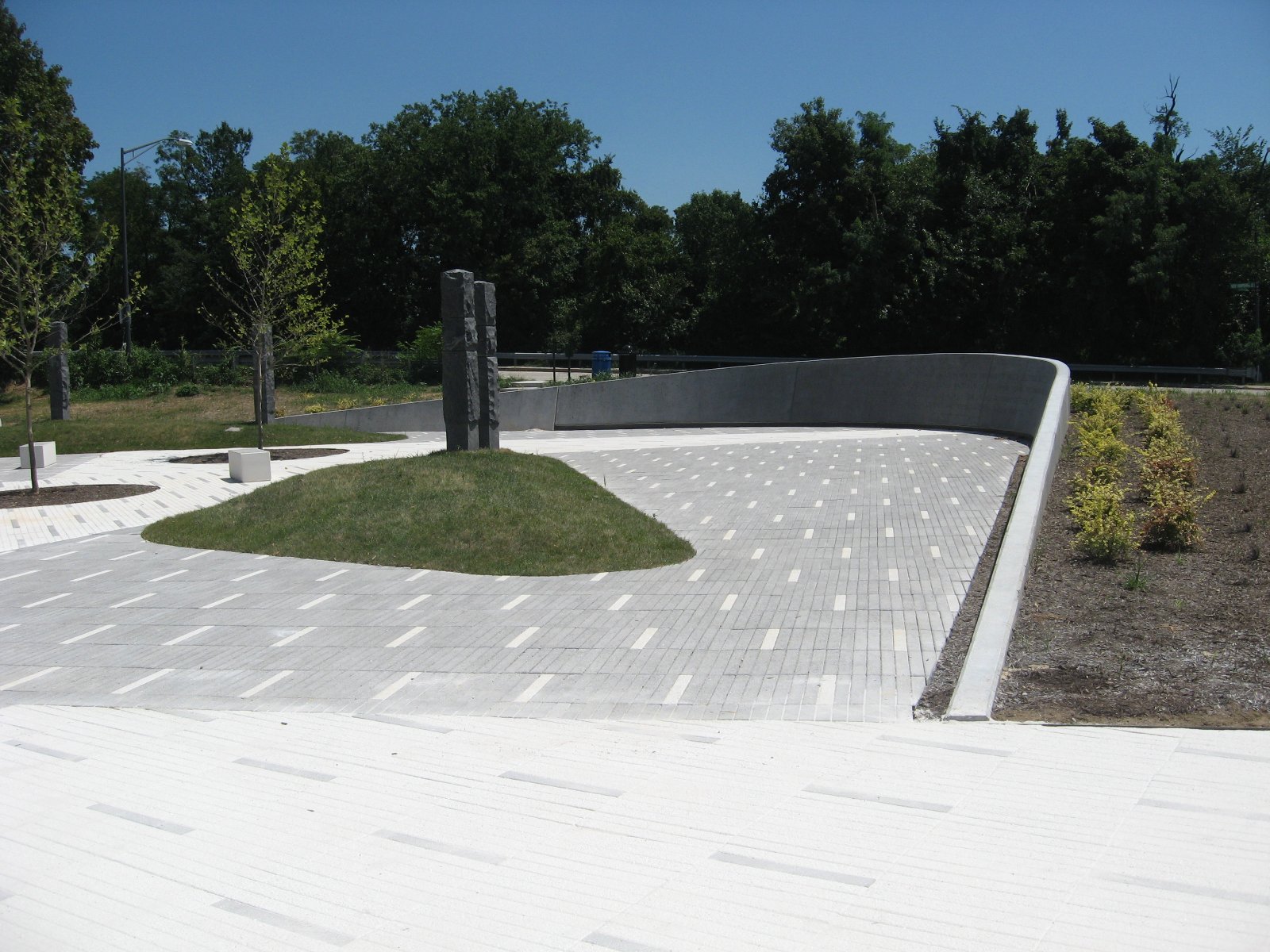 Legacy Memorial Park — curved concrete wall above the gray paving field